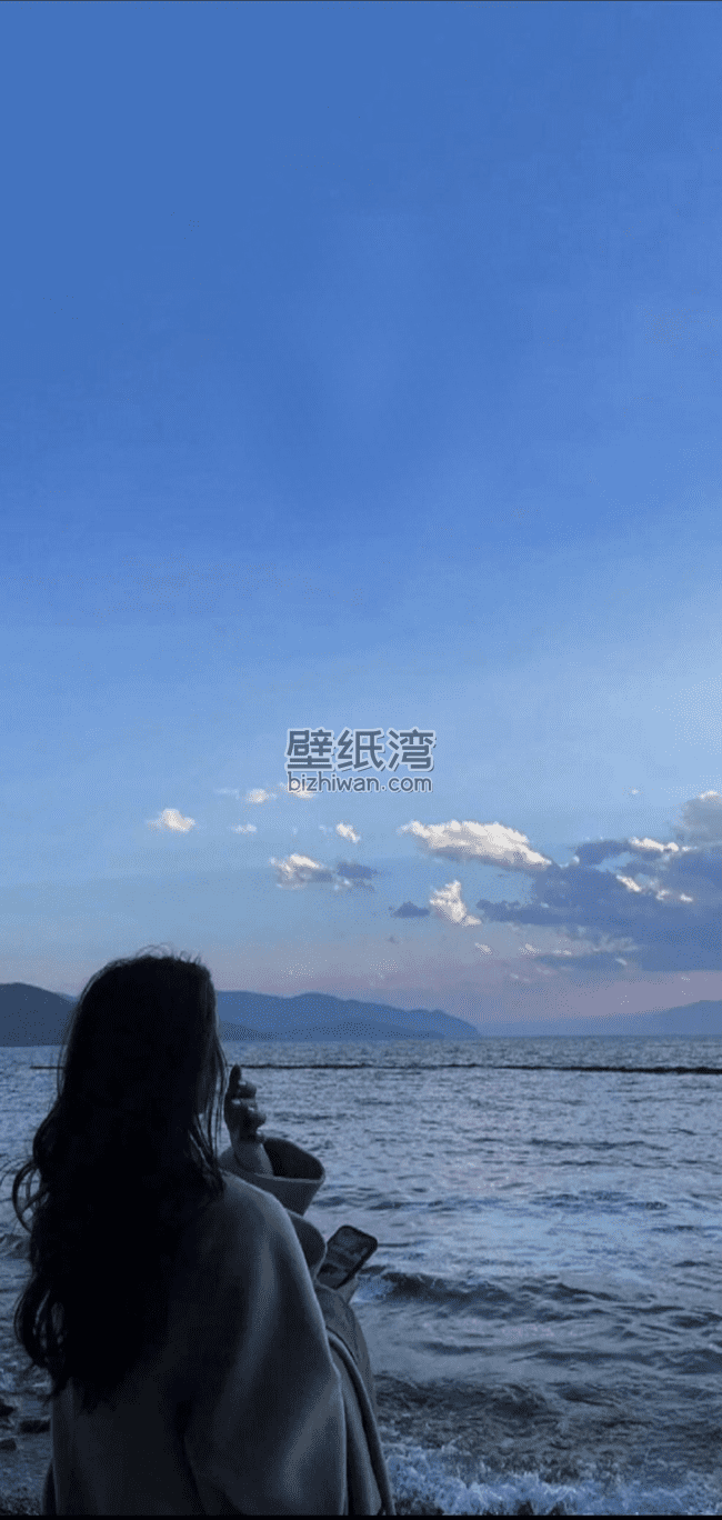 海边穿着大衣的美女背影，远处有山和云朵，手机壁纸图片