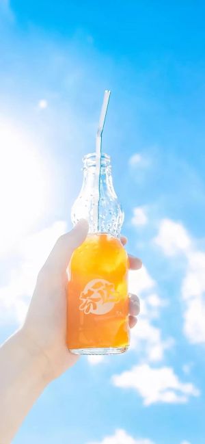 手握装有橙色饮料的玻璃瓶，蓝天白云