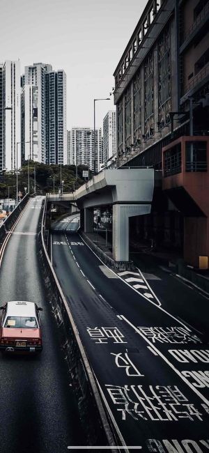 城市高架桥下的道路，两侧高楼林立，红色出租车行驶在道路上,手机壁纸