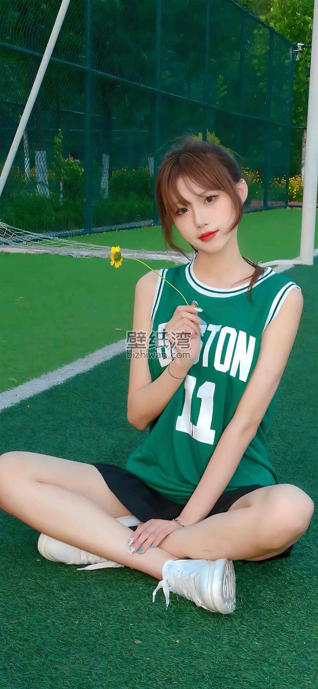 身穿绿色球服的女孩坐在足球场上，手持一朵黄色小花 4K壁纸图片