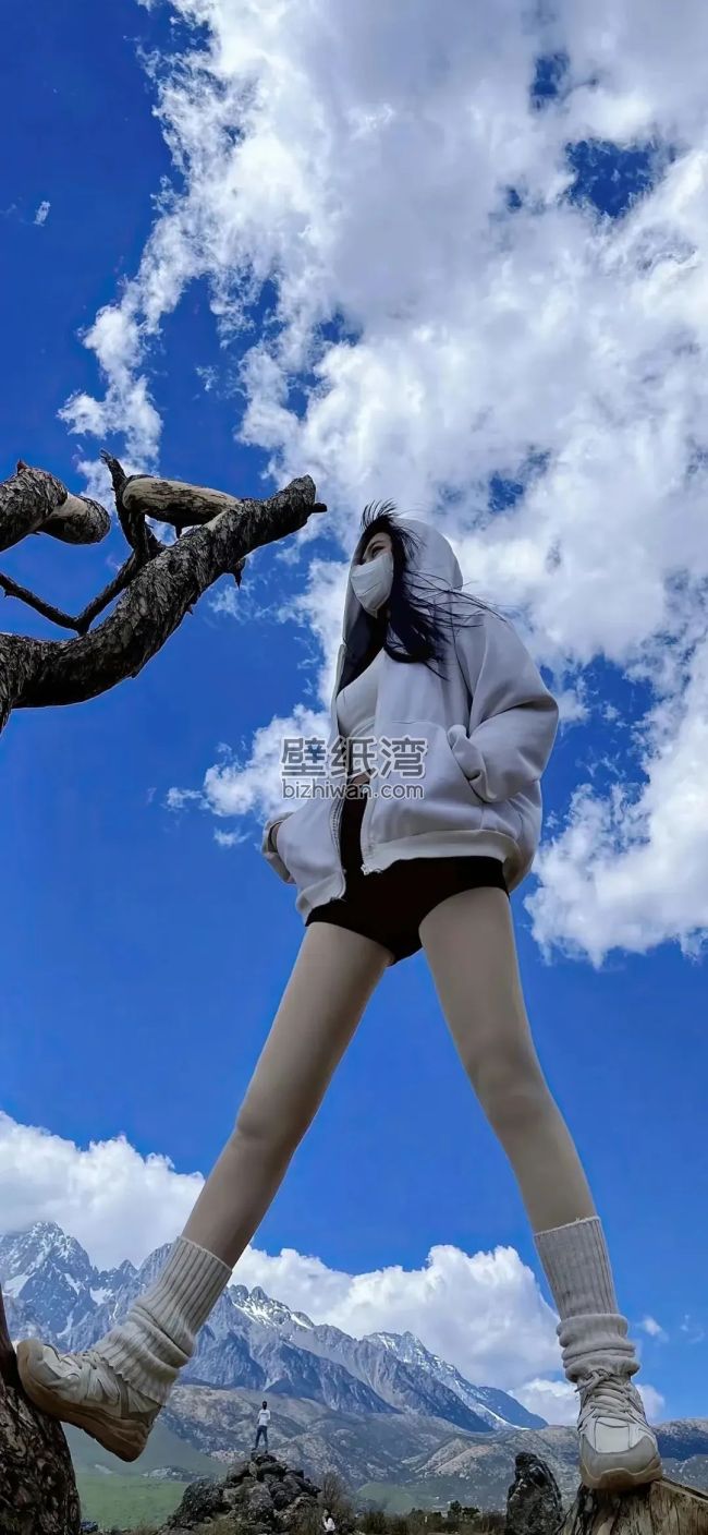穿着短裤戴着口罩的长腿美女站在岩石上，蓝天白云和雪山，手机壁纸