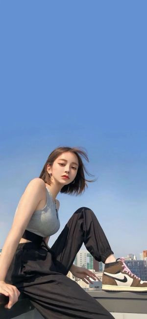 休闲装年轻美女坐在屋顶上，蓝天和城市，手机壁纸图片