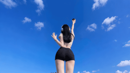 长发美女背影，穿着黑色短裤，戴着耳机，双手举起，站在蓝天白云下 4K壁纸