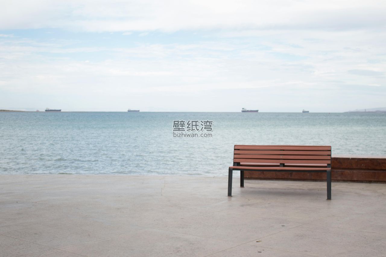 海边的长椅，远处有几艘船只