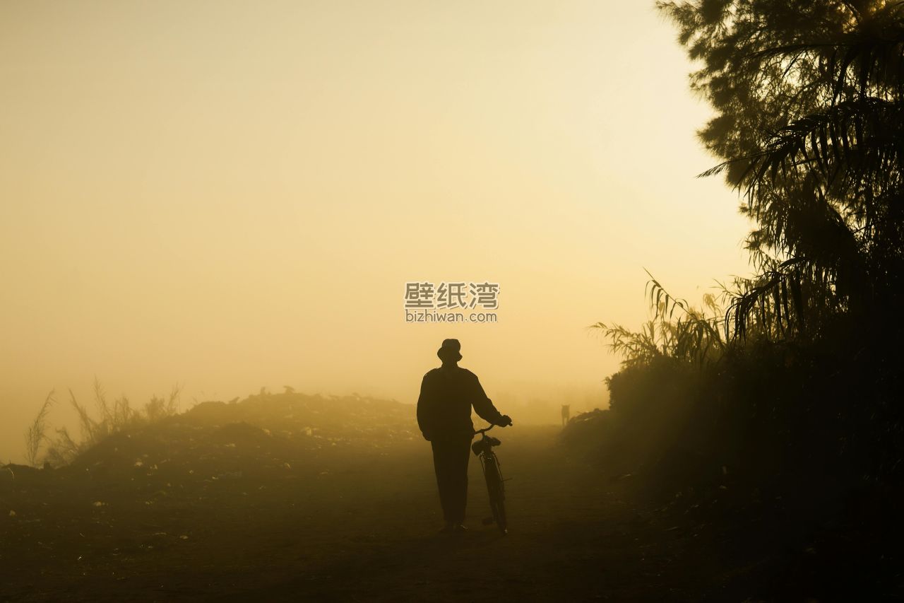 晨雾中的人影站在小路上，手持相机拍摄远方景色
