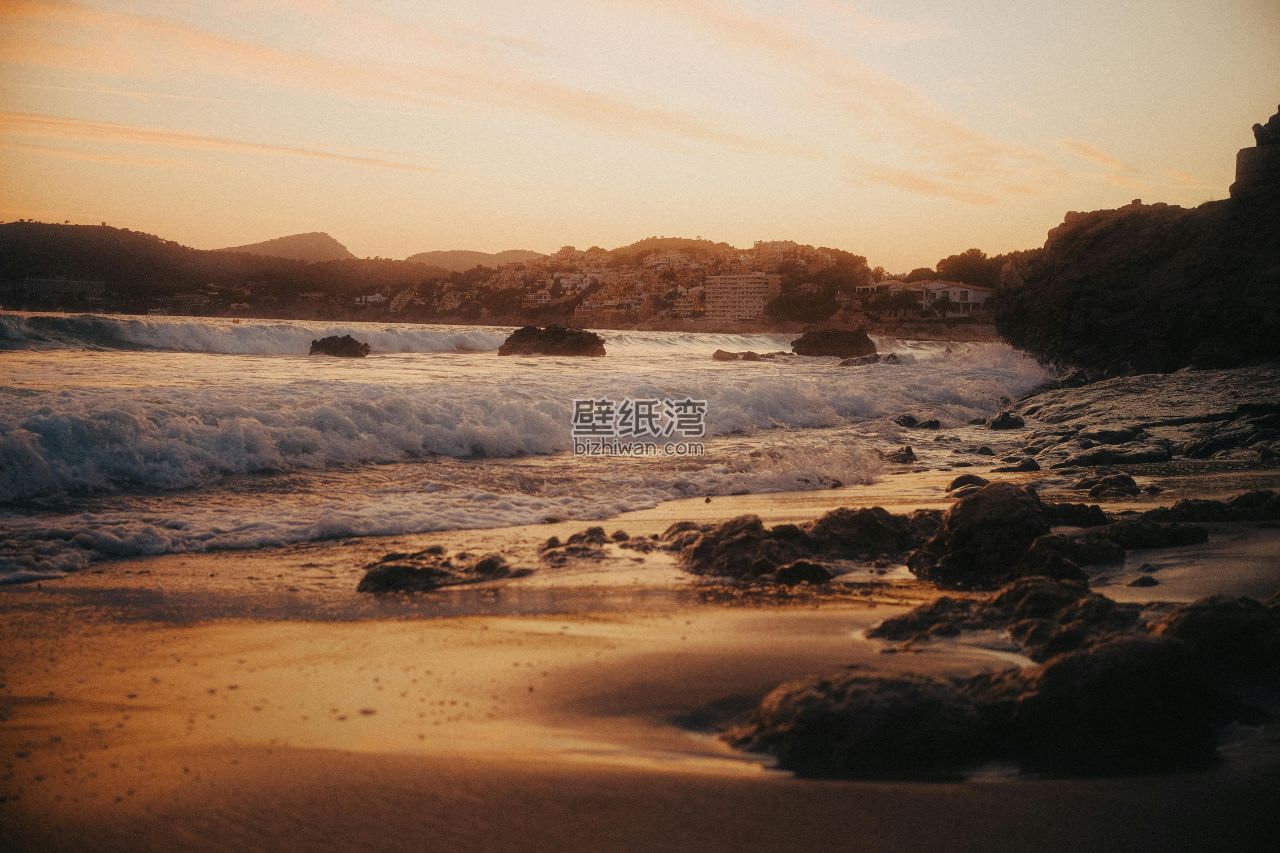 夕阳下的海滩，波浪拍打着岩石和沙滩 6K风景壁纸