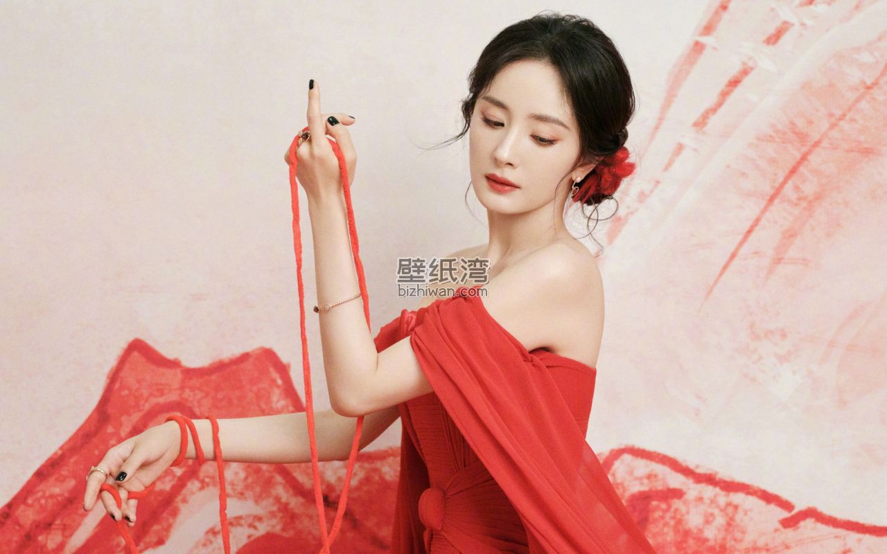杨幂穿着红色礼服，手持红色丝带，背景为淡粉色和红色图案