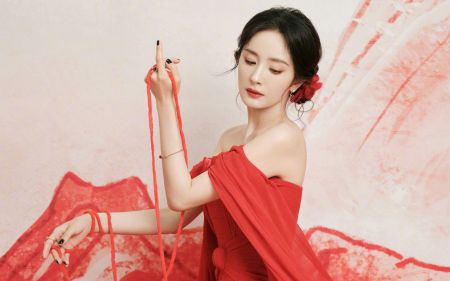 杨幂穿着红色礼服，手持红色丝带，背景为淡粉色和红色图案