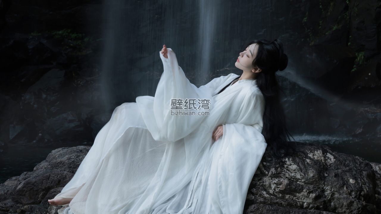 一位身穿白色长袍的女子在瀑布前静坐