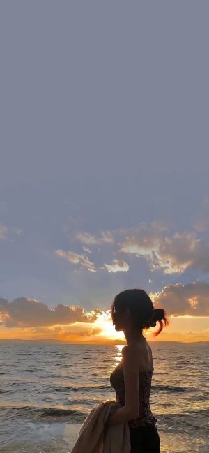 海边日落时分，一位女性站在沙滩上眺望远方