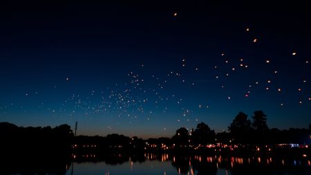 夜晚的天空中飘浮着许多孔明灯，湖面倒映着灯光和树木的轮廓